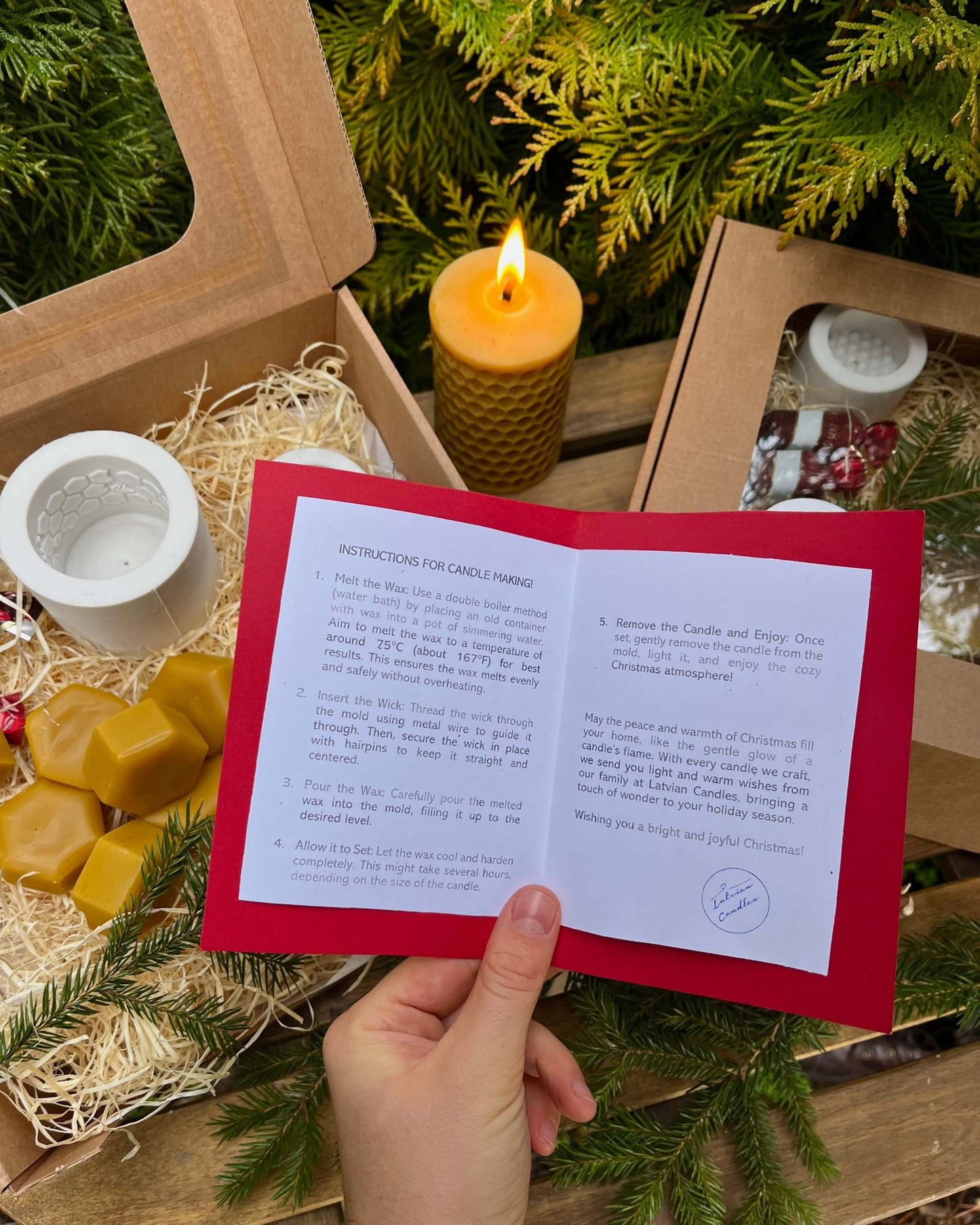 Christmas gift box with candle making supplies, including silicone molds, wax, wicks, and guide, amidst festive decorations.
