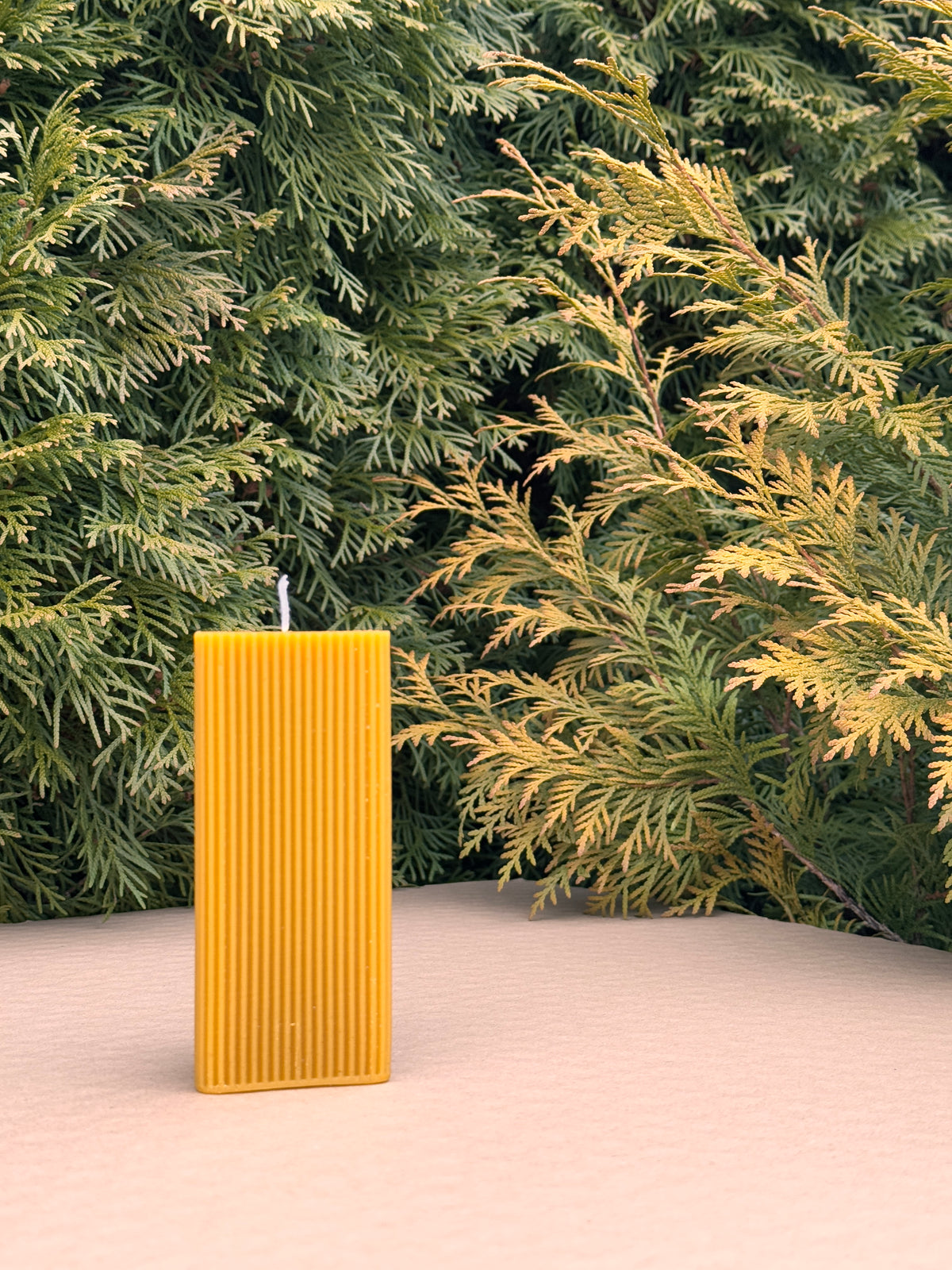 Triangle Fluted Pillar candle viewed flat side on, standing on pink fabric in front of conifers
