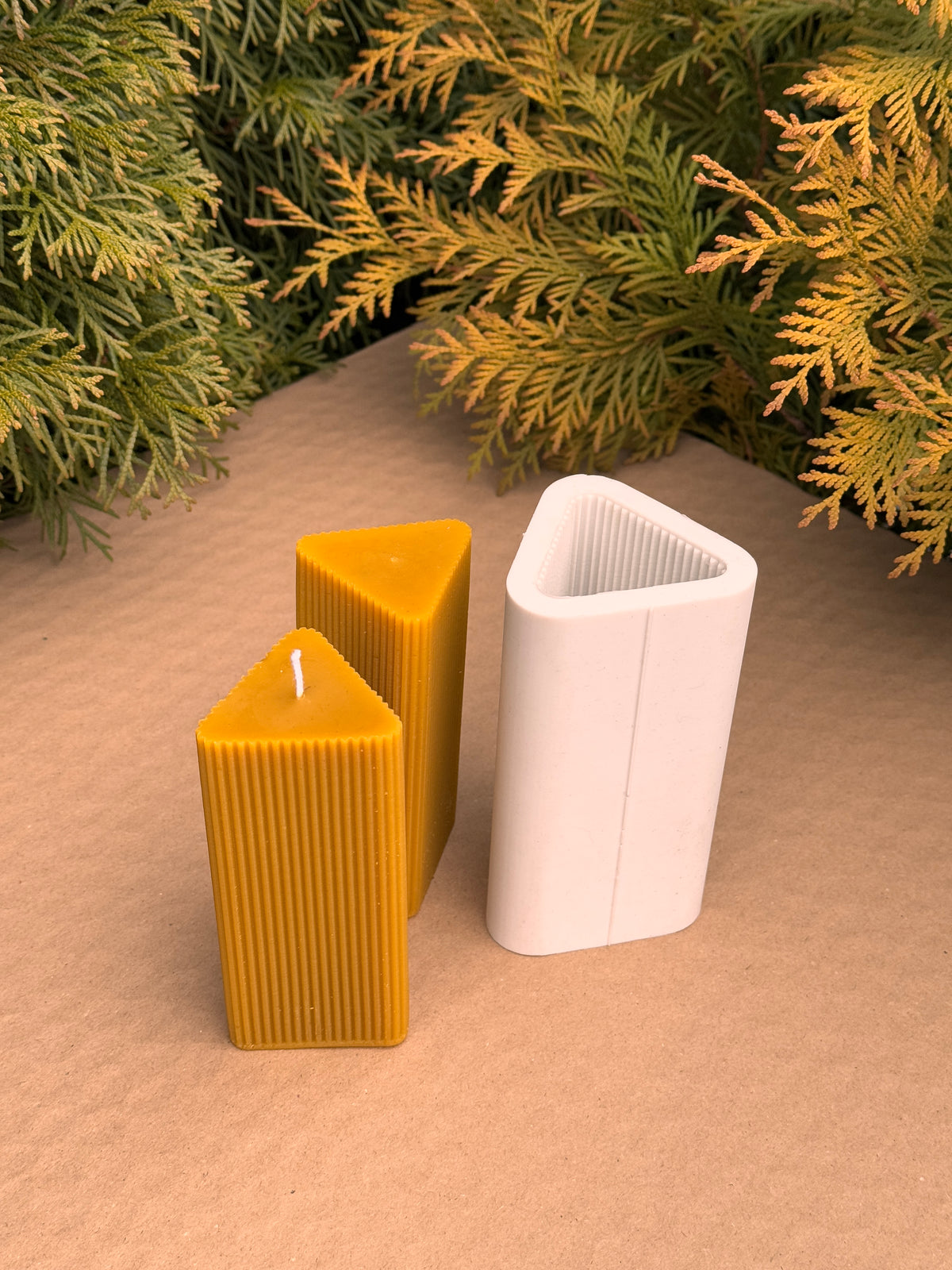 Two Triangle Fluted Pillar beeswax candles next to their upright triangular silicone mould