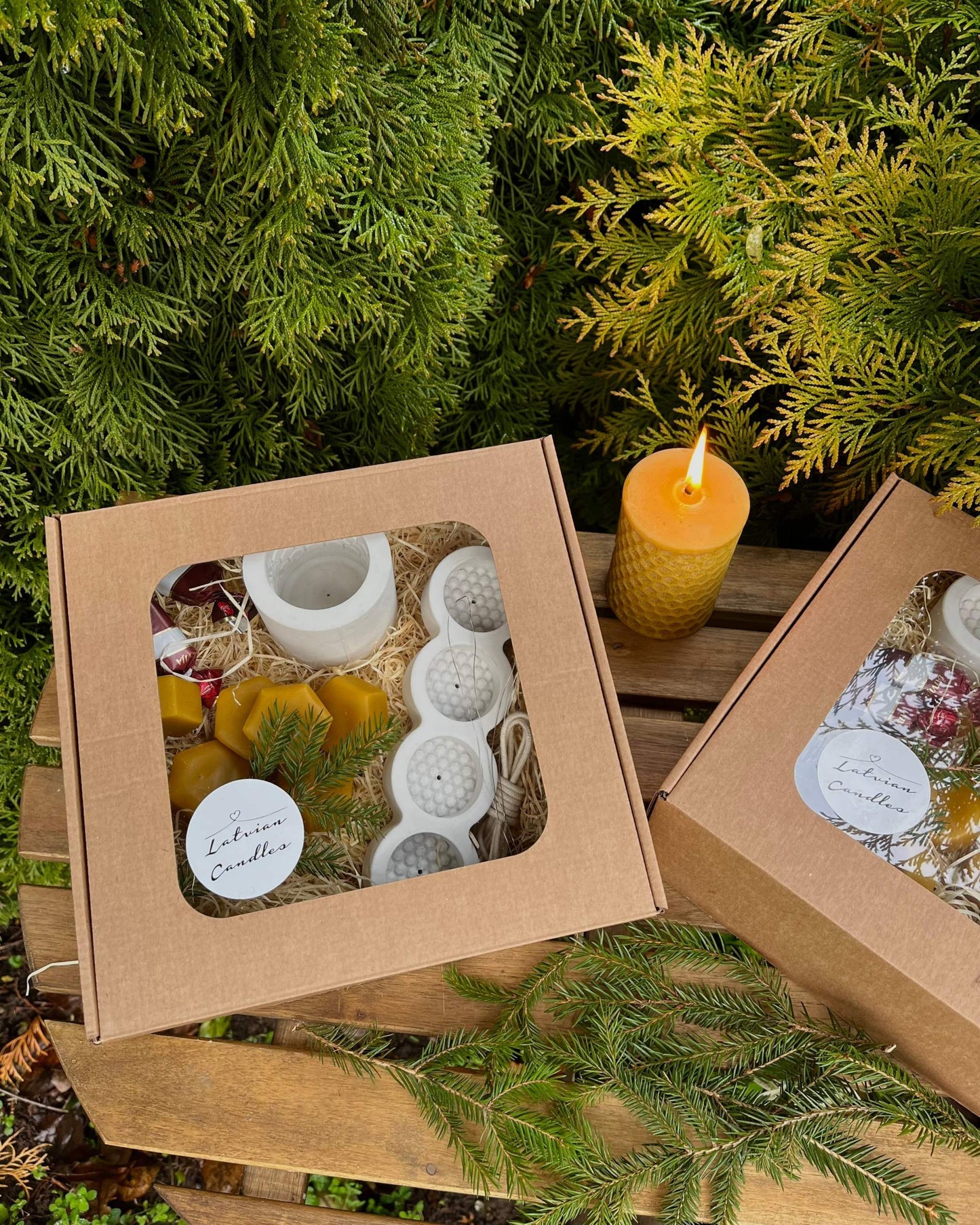 Christmas gift box with candle-making kit, featuring silicone molds, wax, wicks, and Latvian sweets, displayed outdoors.