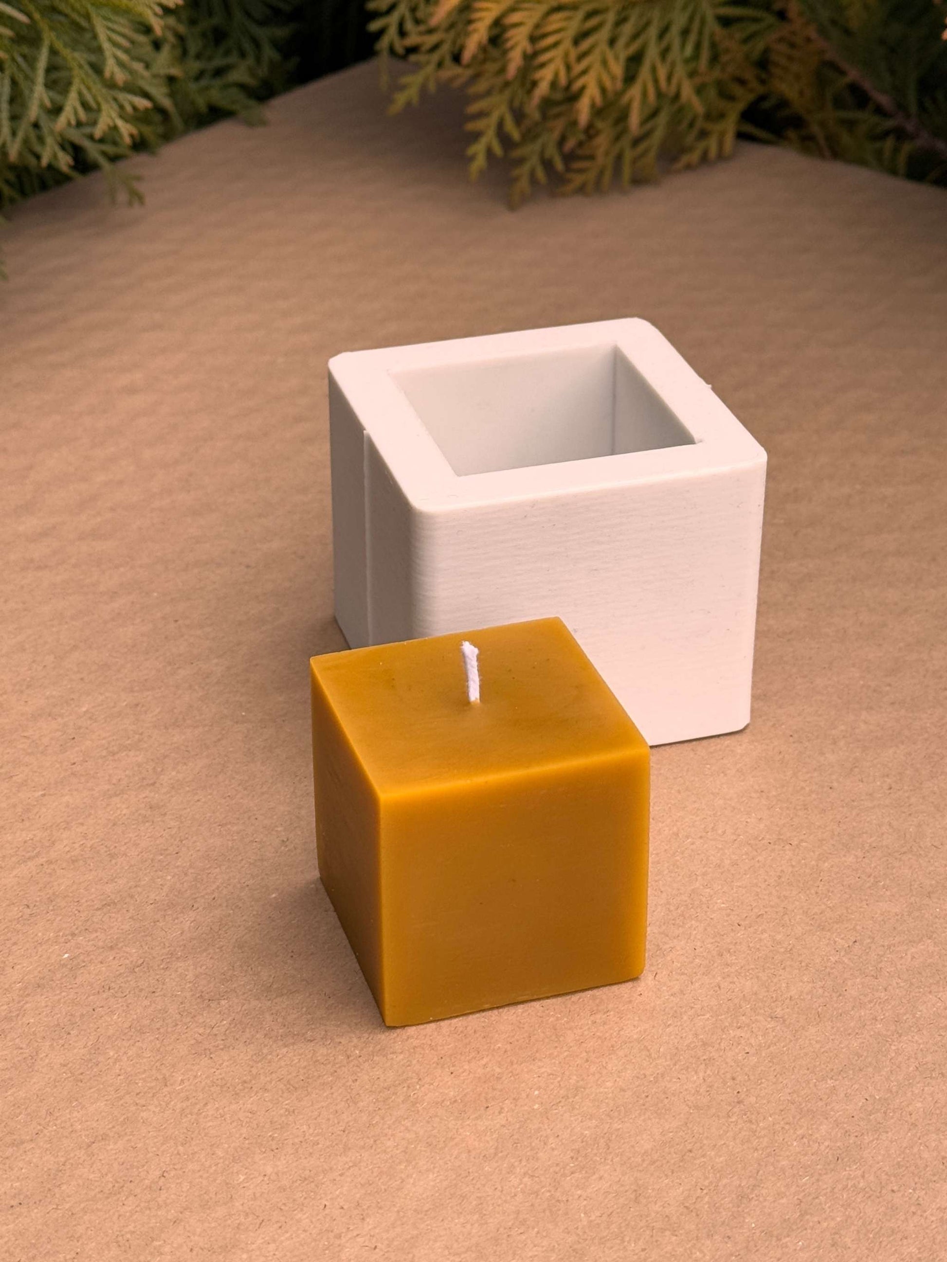 Silicone candle mold with small yellow cube candle on a textured surface.
