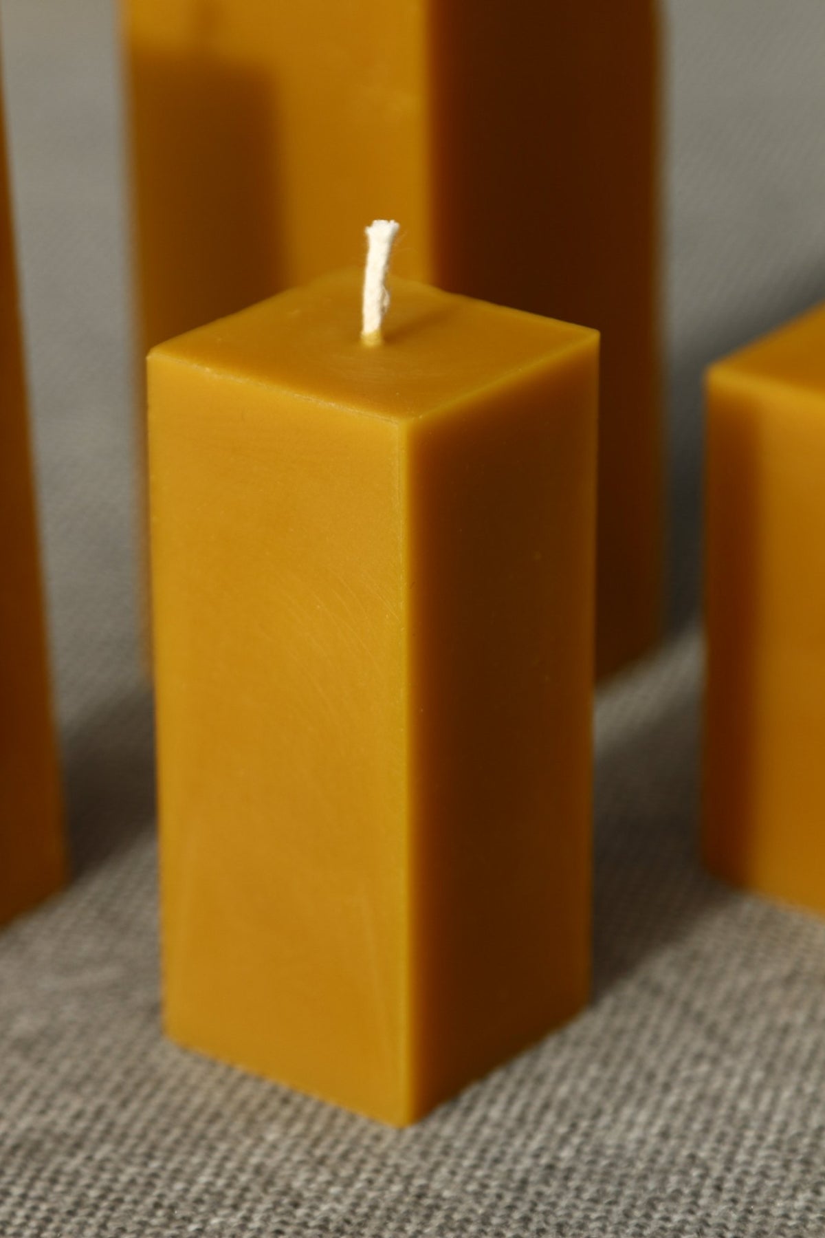 Close-up of a square Cubes beeswax pillar candle with other pillars blurred around it