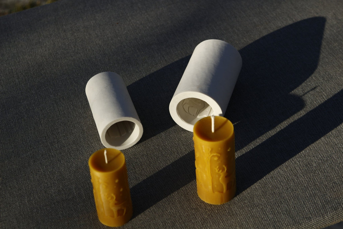 Deers silicone moulds lying on their sides with two beeswax candles leaning in front, top-down angle