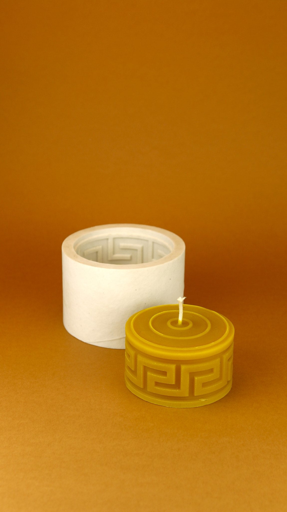 Square Waves beeswax candle in front of its upright silicone mould on an amber background