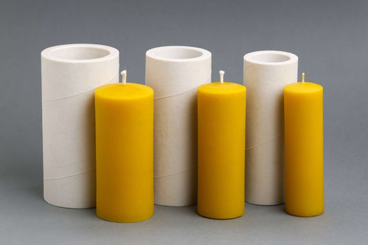 Three plain beeswax pillar candles in front of their silicone moulds
