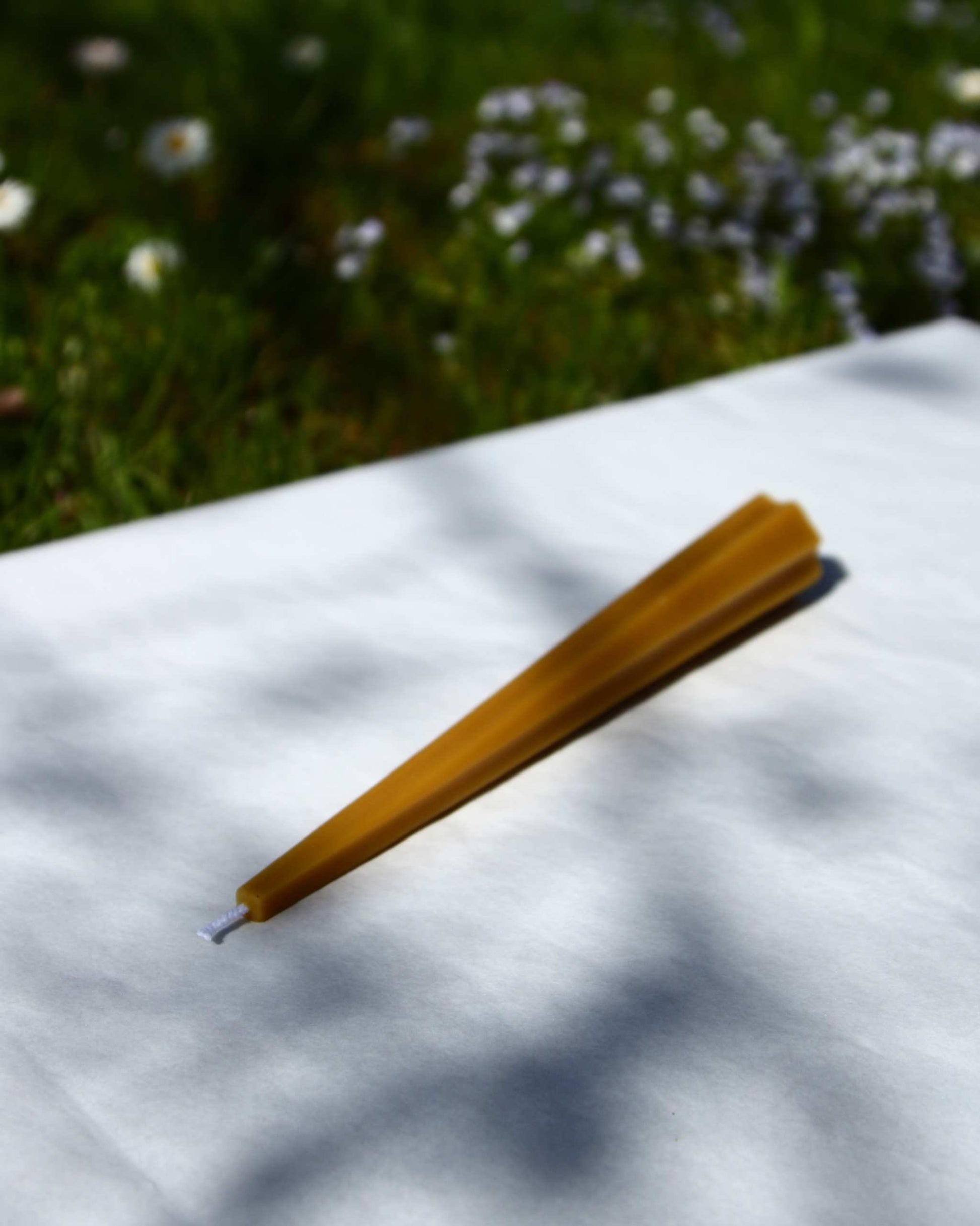Machu Picchu Taper candle on white surface with grass and flowers in background.