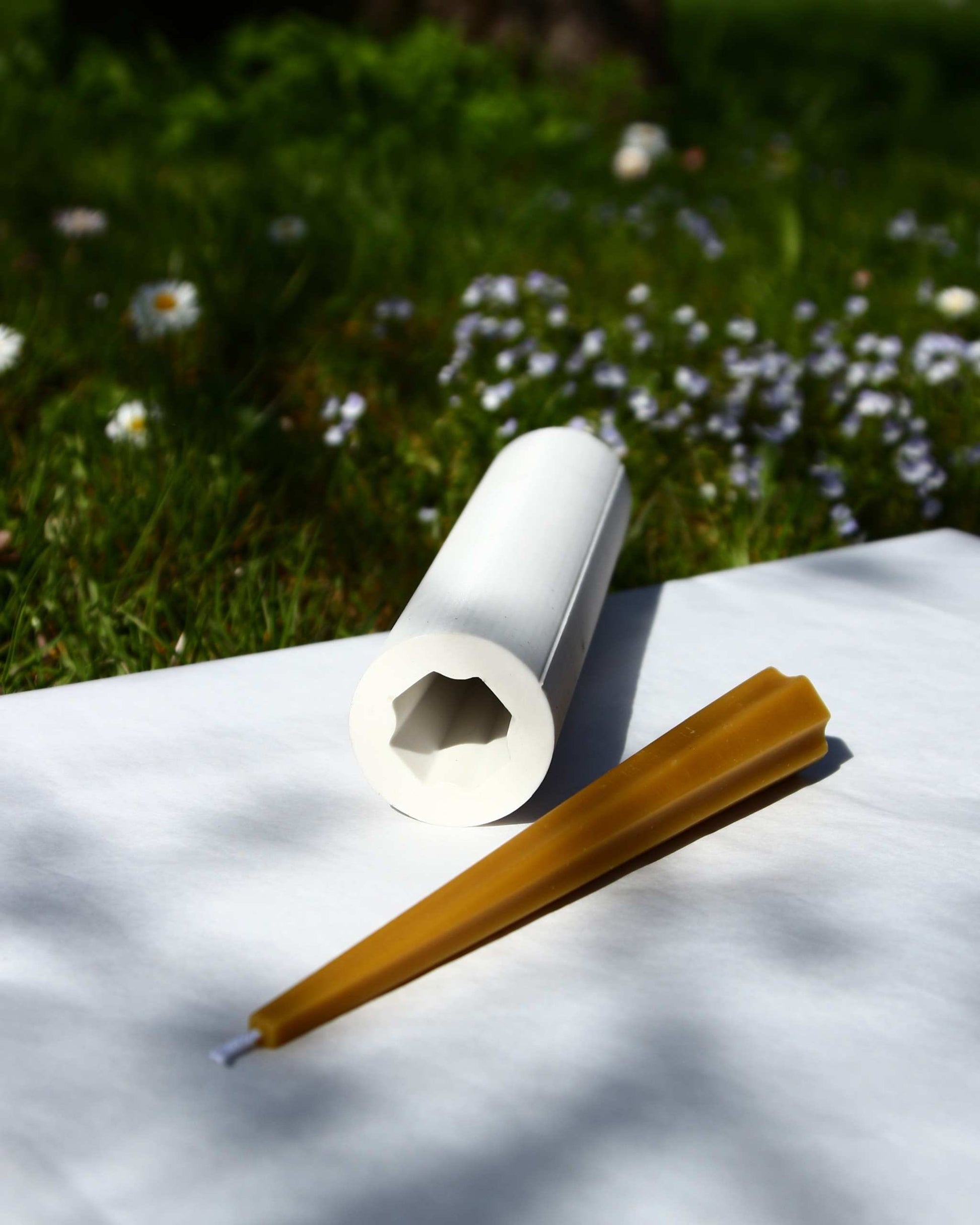 Machu Picchu Taper candle with mold on white surface, surrounded by grass and flowers.