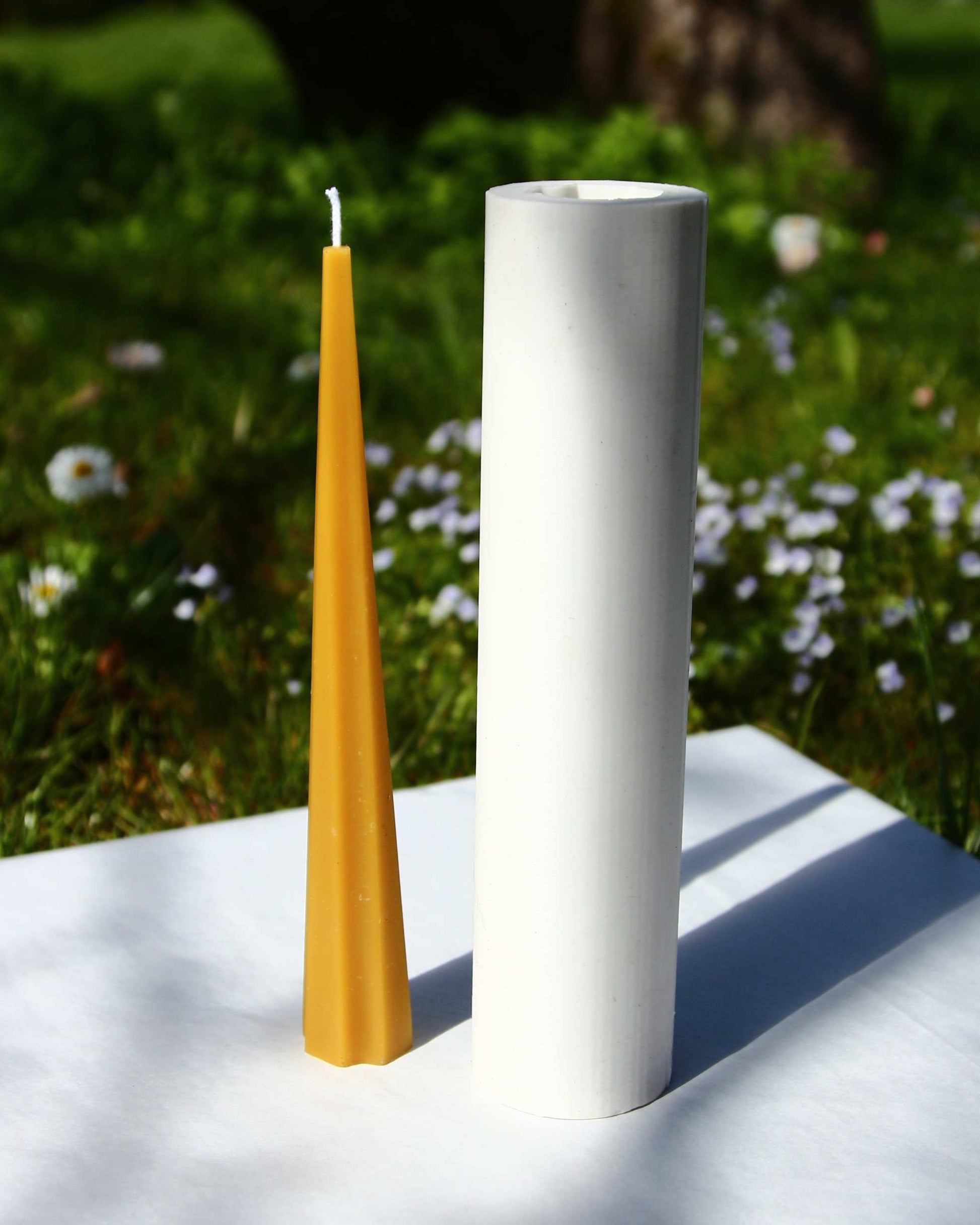 Machu Picchu Taper candle next to a white cylindrical holder outdoors.