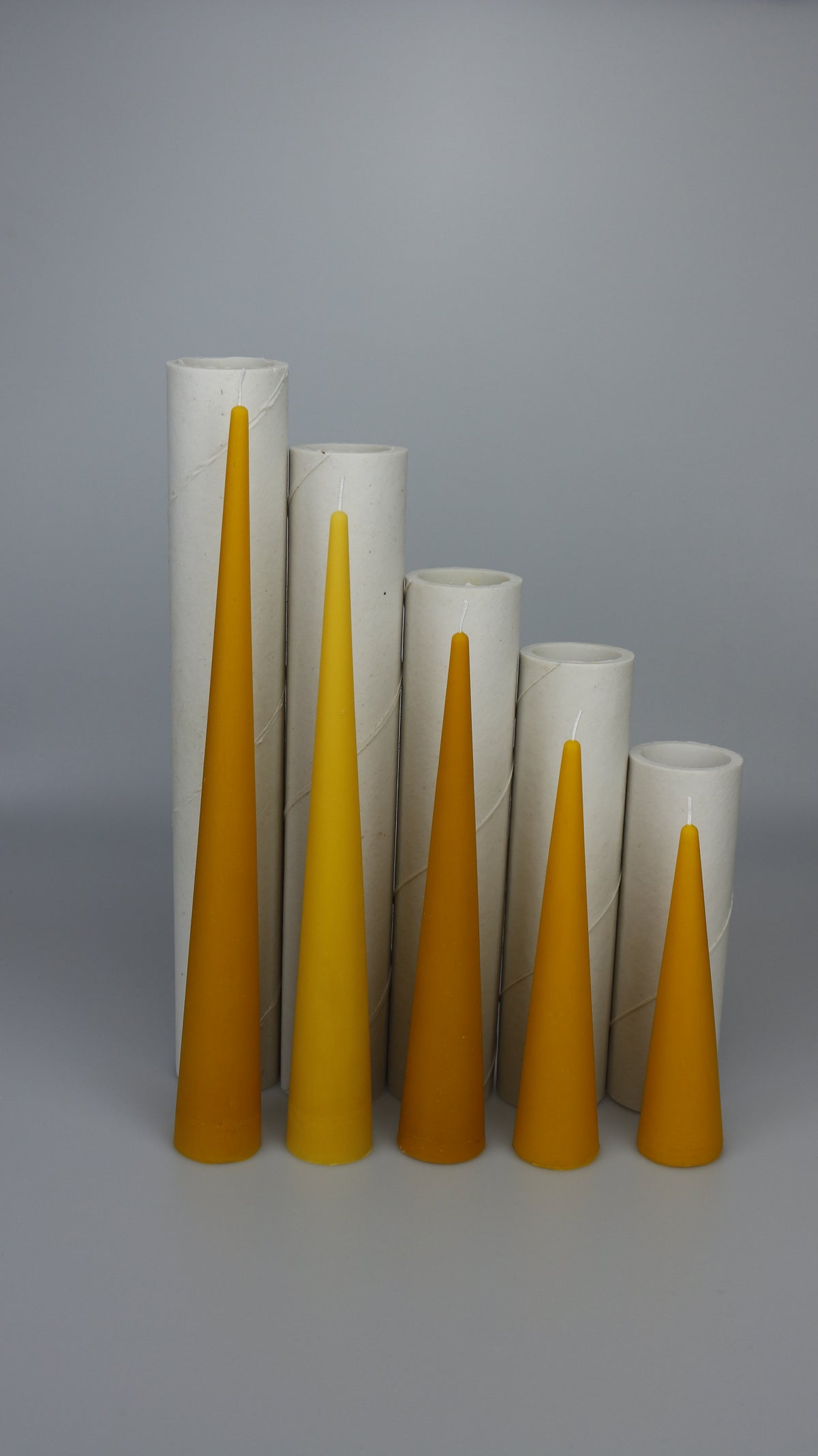 Five beeswax cone candles in front of cardboard display tubes