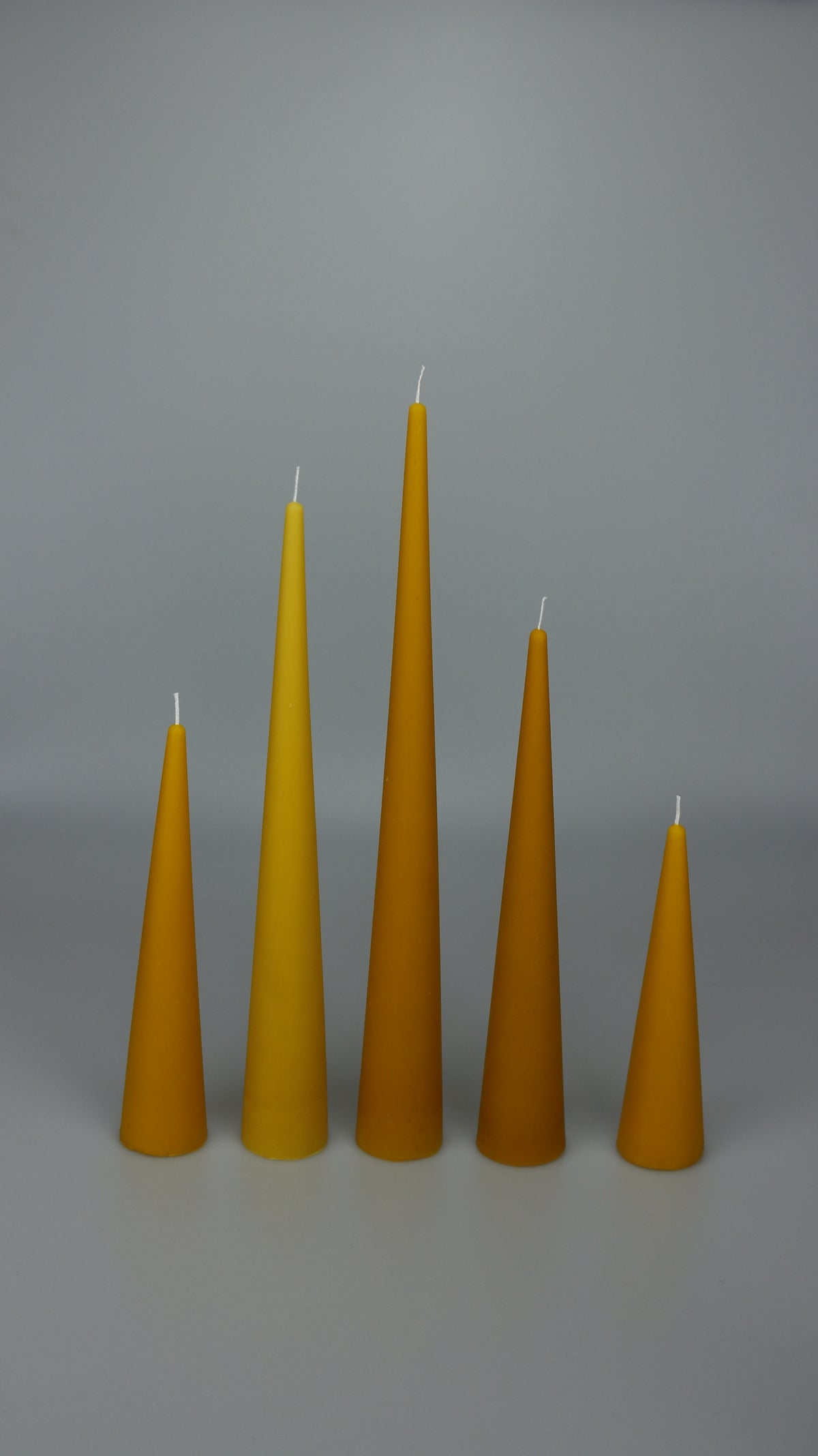 Beeswax cone candles in five heights arranged in a row