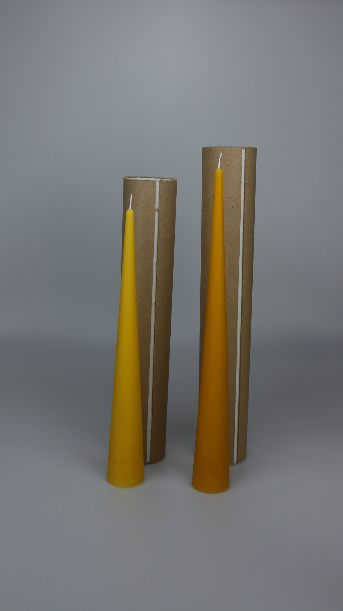 Two beeswax cone candles next to upright cardboard display tubes